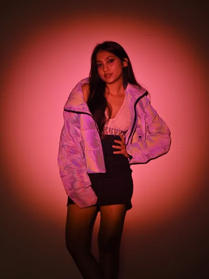 A full-length shot from a studio session, playing with light and shadow. The pink spotlight and iridescent jacket create a cool, artistic vibe.
