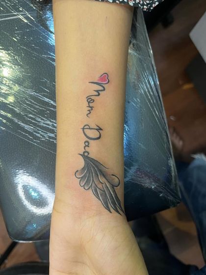 A delicate "Mom Dad" tattoo on the wrist, with a small heart and a single wing. This is a more subtle but equally meaningful tribute.