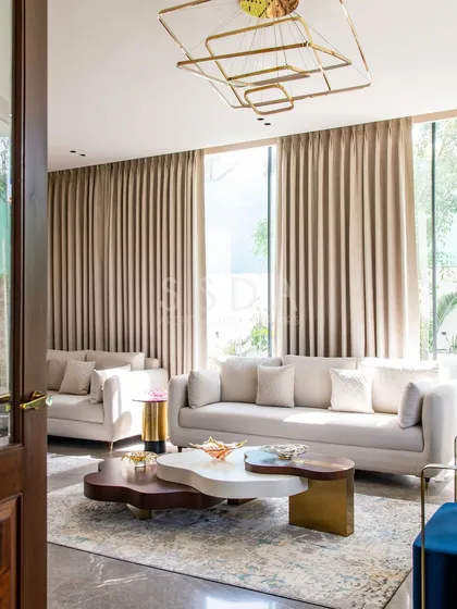 A closer look at the living room in 'House Retold', highlighting the layered coffee tables and the geometric chandelier. The floor-to-ceiling curtains add a sense of height and softness to the modern space.