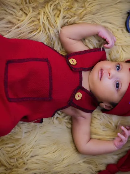 This newborn is awake and curious, dressed in a cute red outfit with a long, pointed hat, lying on a soft fur rug. A great example of capturing those alert moments.
