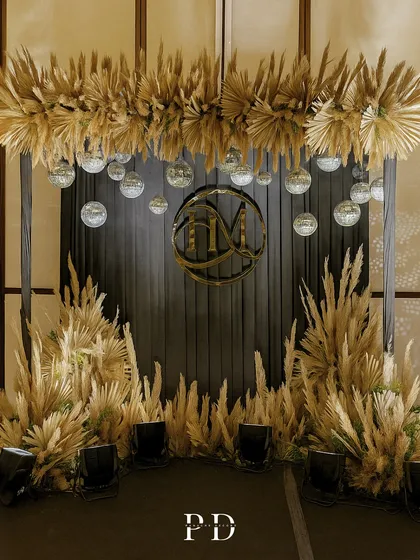 A chic and glamorous photo booth for a Sangeet night. This setup combines a custom gold monogram, sparkling disco balls, and dramatic pampas grass for a look that is both trendy and timeless.