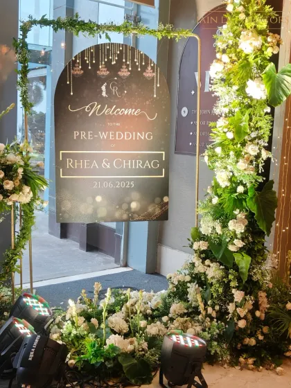 A personalized and elegant welcome for the pre-wedding festivities. The custom signage is framed by a simple golden arch adorned with fresh greenery and white flowers.