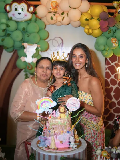 The birthday girl, her mom, and grandmother pose with a spectacular, multi-layered jungle-themed cake, showing that our parties are a true family affair.
