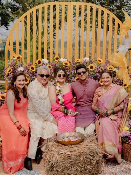 The happy couple posing with their family at the Haldi. The vibrant floral backdrop and rustic hay bale seating create a perfect photo opportunity.