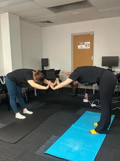 Partner stretches are a wonderful way to build team connection and trust. Here, two participants support each other in a gentle forward fold, helping to deepen the stretch in the hamstrings and back.