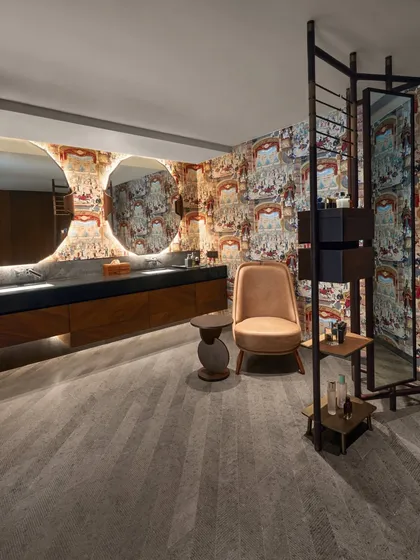 A luxurious bathroom at the Baid Residence featuring Cole & Sons wallpaper and a custom vanity screen. The space is designed as a dressing room and lounge, not just a bathroom.