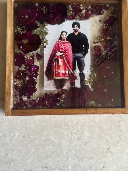 A close-up of a teakwood frame filled with preserved red roses and pearls. The deep colors and classic frame make for a very elegant and romantic keepsake.