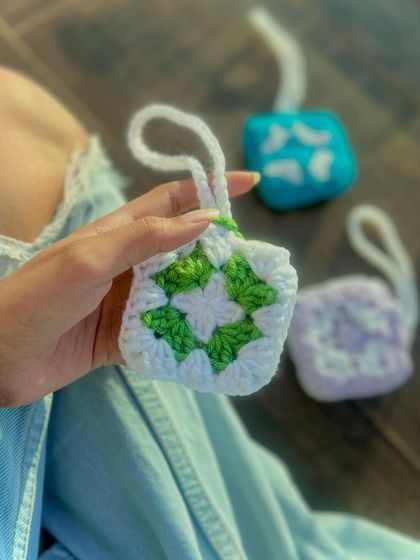 This handmade AirPods pouch features a classic green and white granny square design. It's a stylish way to protect your earphones, with a small loop that makes it easy to attach to your bag or keys.