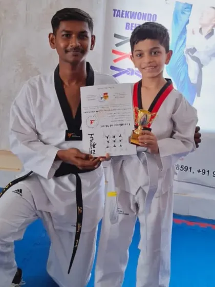 A coach congratulates a young student who has earned his new belt, a certificate, and a trophy for his excellent performance.