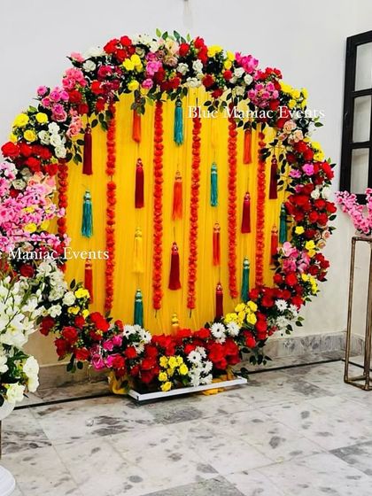 The full view of the circular Mehendi backdrop, flanked by floral stands with cherry blossoms and white gladiolus.