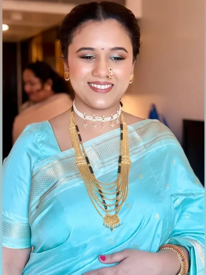 A happy smile showing her complete look, including the traditional Maharashtrian nath and layered gold necklaces.