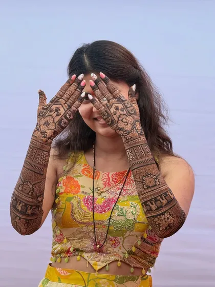 The bride playfully hiding her face, giving a perfect view of her stunning bridal mehendi.