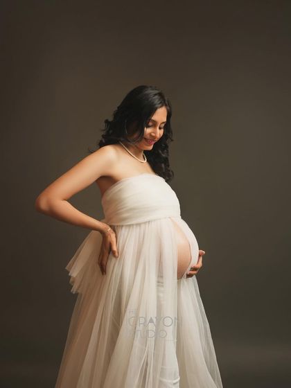 A candid style shot where she is adjusting her dress with a smile. This adds a touch of authenticity and personality to a minimalist and elegant maternity photo series.