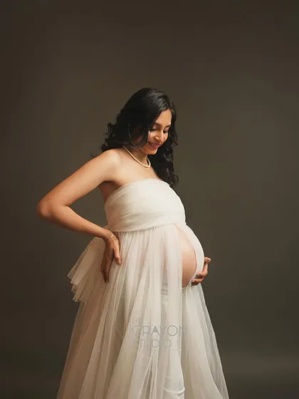 A candid style shot where she is adjusting her dress with a smile. This adds a touch of authenticity and personality to a minimalist and elegant maternity photo series.