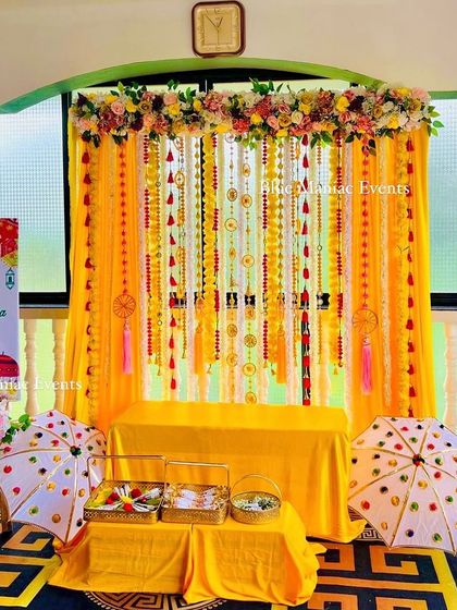 A simple and sweet Haldi setup with a yellow draped backdrop, hanging tassels, and traditional umbrellas. The personalized welcome sign makes it extra special.