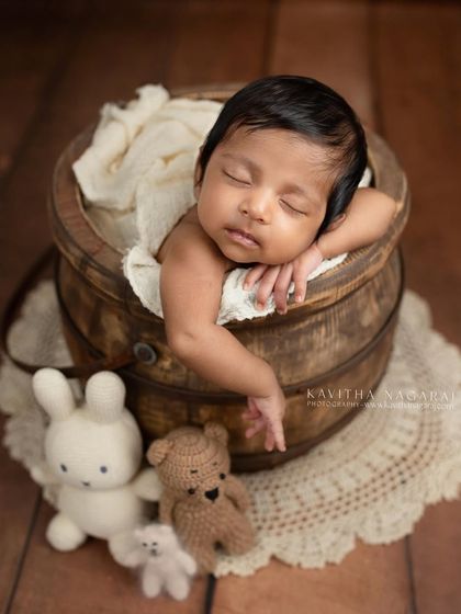 A two-month-old baby rests in a wooden bucket, surrounded by tiny stuffed animals. This shows how we can adapt poses for slightly older babies to create adorable portraits.
