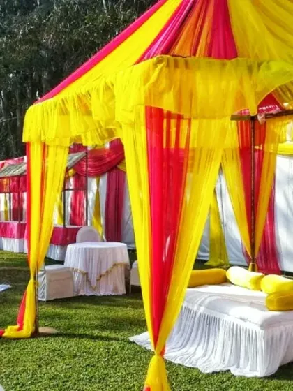 Bright yellow and red tents set up in a garden, with comfortable floor seating, perfect for a vibrant and casual mehndi function.