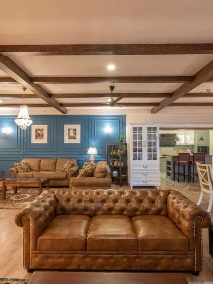 We love blending styles to create unique spaces. This living room combines the warmth of industrial design with classic Victorian elegance, featuring exposed wooden ceiling beams, a chesterfield sofa, and a striking blue accent wall for a truly memorable interior.