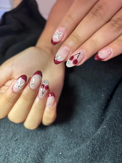 A cute and playful French manicure with a deep red, glittery tip. The design is accented with hand-painted cherries and tiny white bows for a sweet, detailed look.