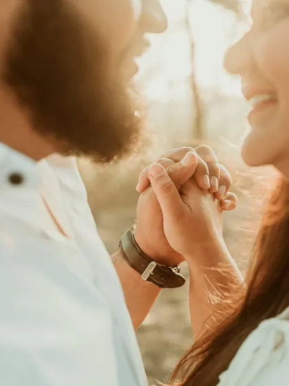 A sun-kissed close-up of a couple holding hands and smiling. The warm golden hour light enhances the feeling of joy and intimacy in this beautiful candid portrait.