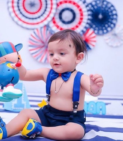 A little boy dressed in a bow tie and suspenders for his first birthday shoot, playing with a toy in a festive setting.