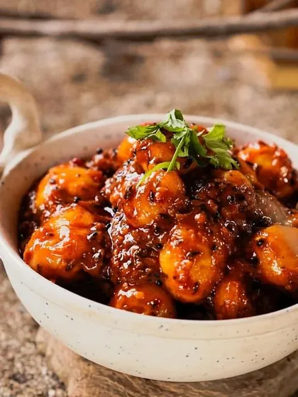 A close-up of the Tamarind Potatoes, showing the rich, dark glaze of the sauce and the fresh cilantro garnish.