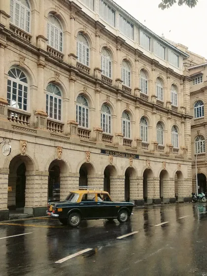 A taxi driving on a wet road in front of a colonial-era building. The elegant arches and the reflection on the street give this photo a timeless, painterly quality.