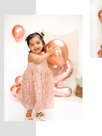 A joyful toddler holds a rose gold balloon during her second birthday photoshoot. The simple, elegant setup with balloons creates a classic party feel.