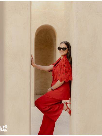 A chic and confident solo portrait of the bride-to-be against minimalist desert architecture in Dubai. Her vibrant red suit and stylish pose make for a stunning, fashion-forward shot.