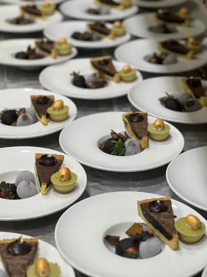 Plated desserts ready for a Christmas event. Each plate features a slice of chocolate tart, a scoop of mochi ice cream, and a pistachio financier.