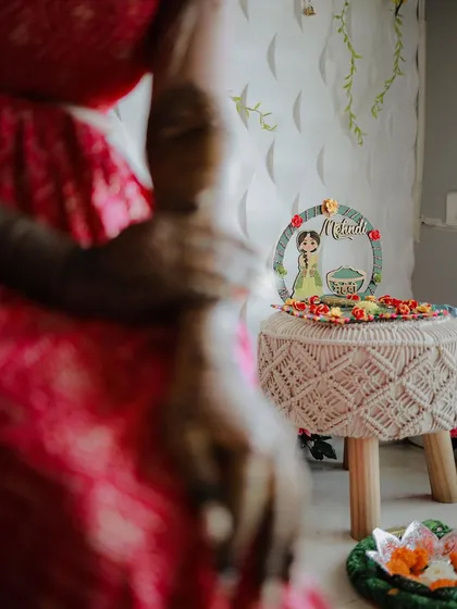 A creative shot focusing on the Mehndi decor. The bride's arm is in the foreground, leading the eye to a cute, personalized sign on a stool.