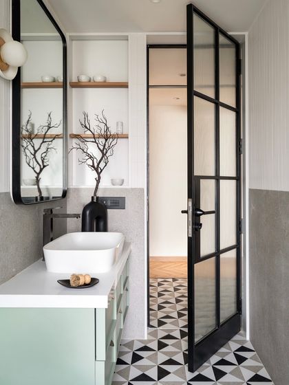 The black metal-framed door with fluted glass opens to reveal the master bathroom. This design element provides privacy while allowing light to filter through, connecting the spaces.