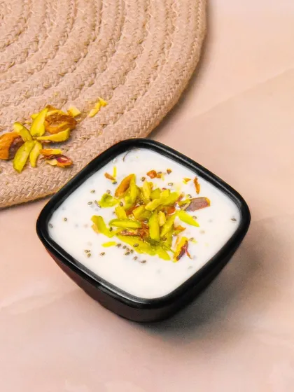 A bowl of honey-flavored Greek yogurt topped with chia seeds and slivered pistachios. The light, warm background gives this healthy dessert a pleasant and inviting feel.