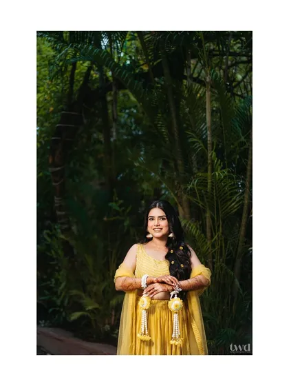 A beautiful portrait of the bride ready for her haldi ceremony. Her yellow outfit and floral jewelry stand out against the lush green background, making her look like a forest nymph.