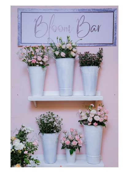 The setup for our Bloom Bar, featuring a variety of fresh flowers in white tins against a pink backdrop. The simple, elegant presentation is both beautiful and functional.