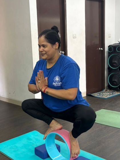 A student works on balance and stability, using a yoga wheel and blocks to challenge her focus in Malasana (Garland Pose).