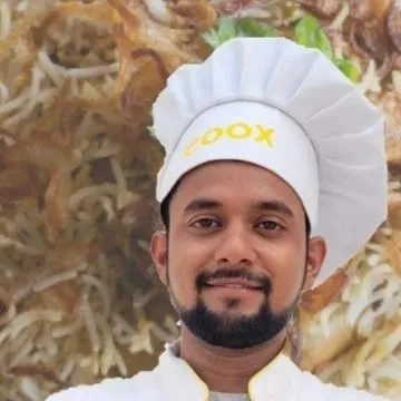 A smiling chef in our signature COOX uniform, specializing in Mughlai cuisine. He is ready to prepare authentic, flavorful dishes like biryani for your event.