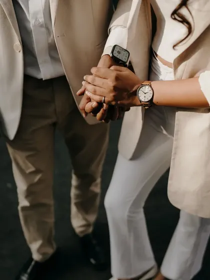 A detail shot focusing on the couple holding hands, showcasing their engagement rings and coordinated watches. It's the little details that tell a big story of commitment.