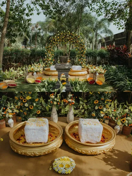 A wide shot of the stunning outdoor Haldi decor, with a seating area surrounded by lush greenery and vibrant yellow flowers.