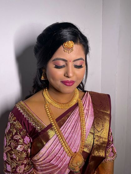 A soft glam bridal look with a focus on pink tones. The shimmery pink eyeshadow and matching lip color create a cohesive and romantic look that pairs beautifully with her silk saree.