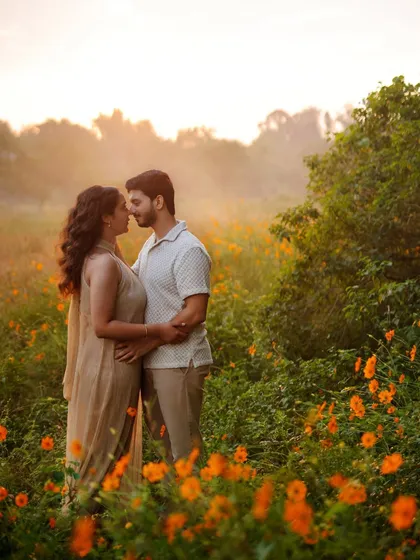 A beautiful, wide shot of the couple in a field of flowers during their pre-wedding shoot. The soft, golden light and natural setting create a dreamy atmosphere, perfectly complementing their relaxed, coordinated outfits.