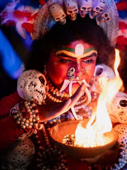 Another angle of the Kali performer, this time focusing on the interaction with the sacred fire. The lighting highlights the detailed makeup and skull decorations.