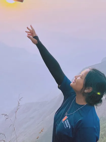 A traveler reaching for the sun at a beautiful sunrise point in Munnar.