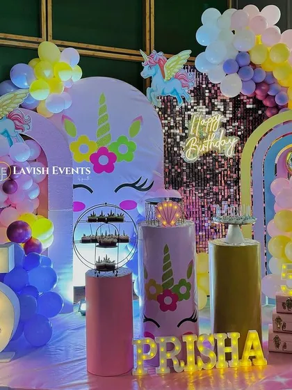 A vibrant and magical unicorn-themed party with a shimmery backdrop, rainbow balloon arches, and a large light-up number '5'.