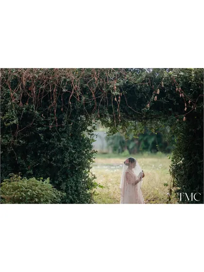 A beautiful solo portrait of the bride-to-be, seen through a natural archway of foliage. The veil adds a touch of softness and anticipation, making for an ethereal and timeless bridal shot.