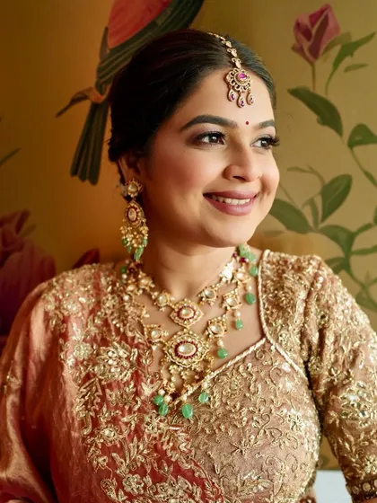 A close-up portrait highlighting the beautiful jewelry and the complementary makeup. The green in the necklace is subtly echoed in her overall warm, peachy tones.