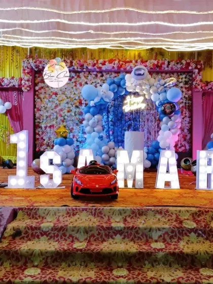 A spectacular stage decoration for a first birthday party. This grand setup includes marquee letters, a full backdrop with a balloon arch, and a toy car for a dramatic entrance.