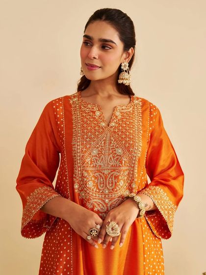 A close-up of the orange kurta, highlighting the detailed paisley and floral embroidery around the neckline.