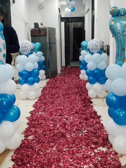 A 'Welcome Baby' home entrance with a red rose petal carpet and blue and white balloon pillars on either side.