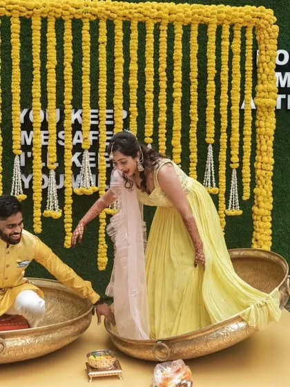 The couple seated in large traditional 'urli' pots for their haldi, a unique and fun setup.